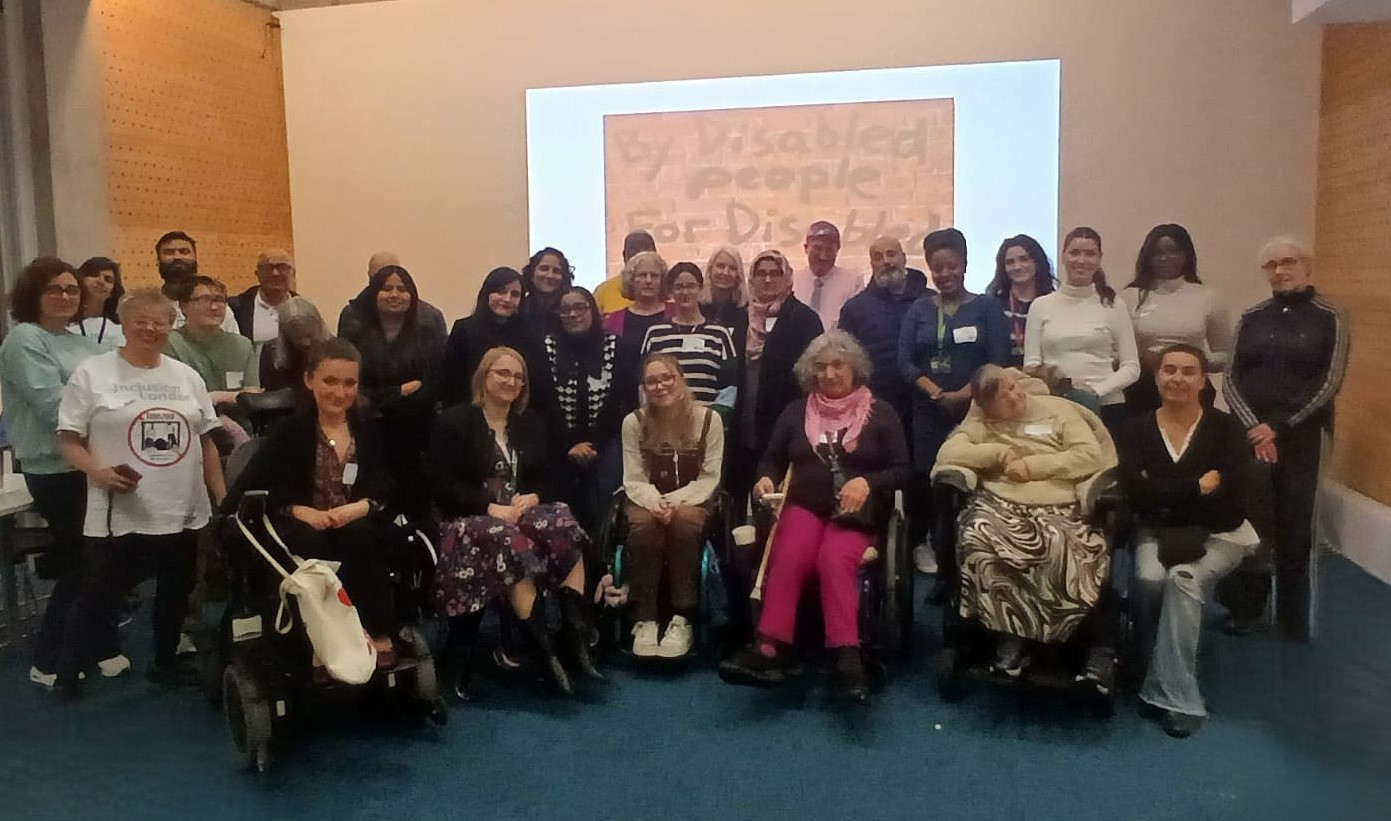A photo of attendees from the Inclusion London Event. There is a diverse group of around 30 people, all smiling at the camera.